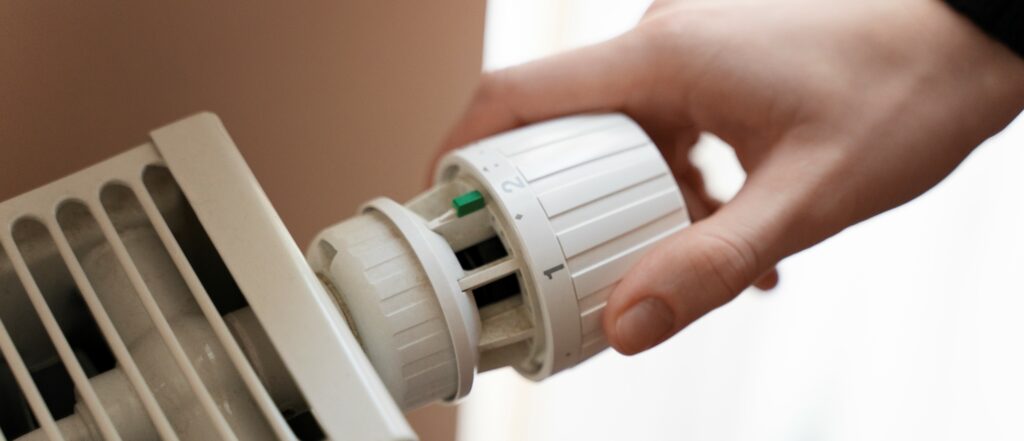 Immagine di una mano che regola la temperatura del termosifone tramite la valvola termostatica